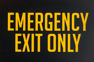 emergency exit only yellow vinyl sticker text Information sign on a black door, industrial room symbol, selective focus and close up view