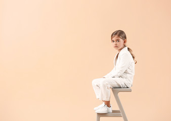 Cute little girl in autumn clothes sitting against light background