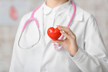 Female cardiologist with red heart on light background