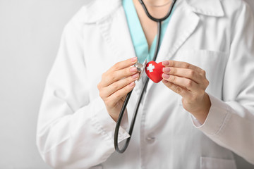 Female cardiologist with red heart on light background, closeup