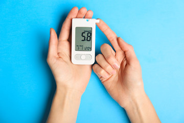 Hands of diabetic woman with digital glucometer on color background