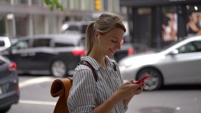 Slow motion effect of happy female tourist with backpack checking email while download new music for listening on leisure during vacations, cheerful woman chatting via cellphone