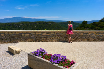 Beautiful young woman standing at viewpoint in front of flowers in the Provence South France looking at landscape and nature