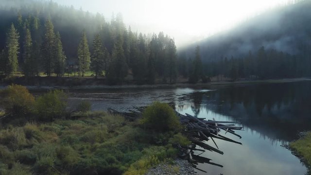 Aerial flying over the Lochsa river, stacked up tree logs and forest. Morning fog covering the the hills. Nez Perce Clearwater National Forests, Idaho, USA.