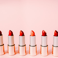 Multi-colored lipsticks stand in a row on a pink background. The concept of different, collections and beauty. Red, pink and burgundy lipsticks