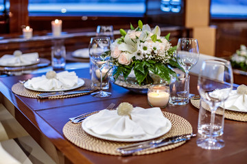Selective focus shot of the dinner table with plates and wine glasses on the yacht