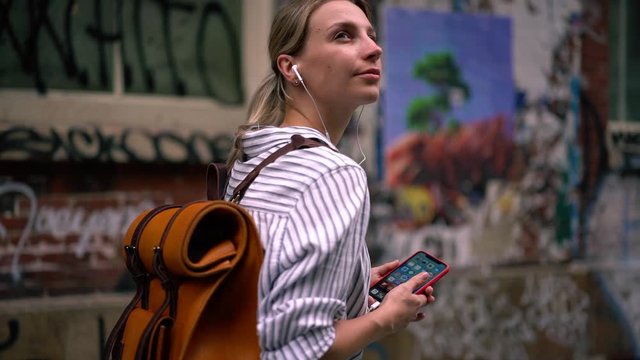 Vacation lifestyle, slow motion effect of attractive Caucasian hipster girl in electronic headphones listening audio guide during time for exploring new city