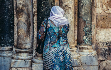 Fototapeta na wymiar Woman prays in front of the wall of Church of the Holy Sepulchre located in Christian Quarter of Jerusalem, Israel
