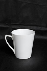 A white porcelain cup is isolated on a black background.