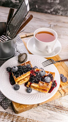 Vertical food banner. Viennese waffles with blueberries and jam and a cup of tea. Dessert. Homemade baking.