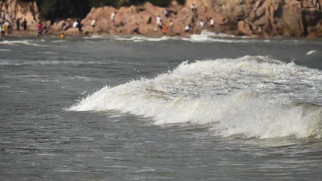 Close up of wave on muddy beach with crowded tourists background, camera pan, high speed, super slow motion, 180 FPS.