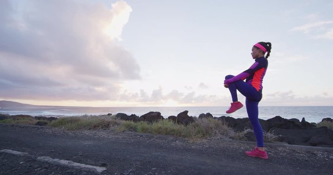 Leg stretching exercise fitness runner woman doing running warm-up, glute and hamstring muscles stretch standing wtih single knee to chest stretch. Female athlete preparing legs for cardio workout.
