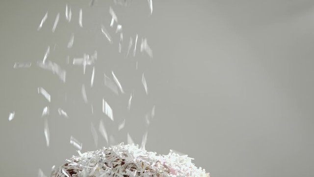 Shredded secret documents falling through the frame onto a pile of shredded paper against a white background.