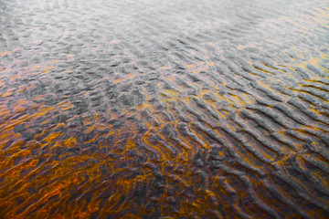 Tidal beach at low water (low tide or ebb) with ripples in the sand and the sky reflected in shallow water.