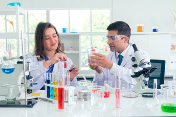 Adult caucasian woman and man chemist in protective glasses looking at microscope against chemistry lab background. Medical analysis processing concept.