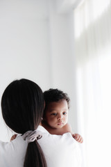 asian mother holding her black mixed race baby girl in white room