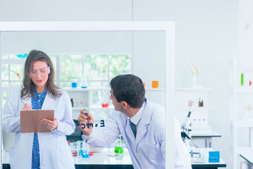 general-view of two people studying and testing substances in a lab with lab tools and colorful liquids and a blackboard with chemical formulas on the background