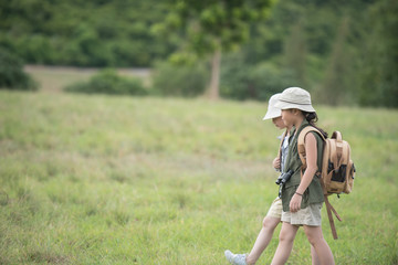 Naklejka na ściany i meble Two little girl carrying a backpack and wearing a hat. Running around in the grassland Children walk and enjoy the surrounding nature. She enjoys traveling in the summer. travel and adventure concept.