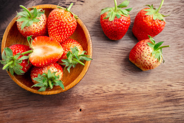 Top view group of fresh berry fruit, red strawberry in a brown wooden bowl and a half sliced on wooden background with copy space