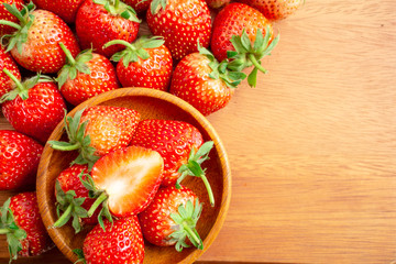 Top view group of fresh berry fruit, red strawberry in a brown wooden bowl and a half sliced on wooden background with copy space