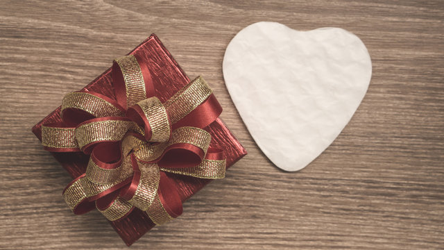 Red gift box with golden ribbon and white heart paper cut for surprise valentines day present on brown wooden background, top view photo