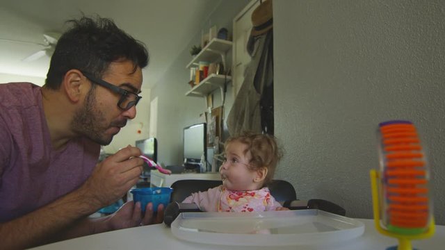 Beautiful shot of father playing with baby daughter as he feeds her with spoon