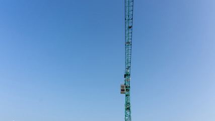 Upward view of the large tall Tower Crane, moving machine and building in construction work, scaffolding on the top floor, under white fluffy cloud clear blue sky