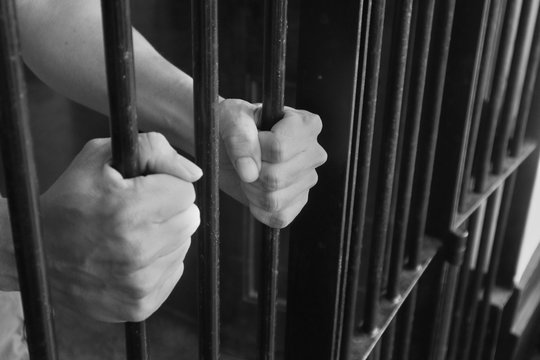 Prison Cell Bars.Hand of the prisoner holding steel lattice jail bars.Criminal justice imprisonment concept.