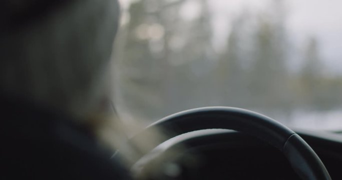 Handheld medium close-up 4K shot with shallow depth of field of woman in wool headband and winter jacket driving car in winter landscape in sunset, in Oslo Norway. Shot on professional cinema camera.