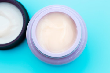 Jar with white cream and lid on blue background, top view, copy space
