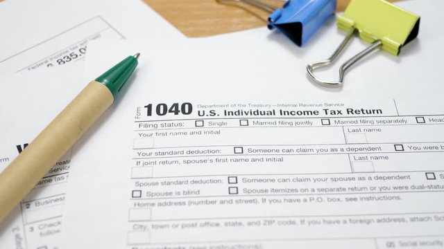 Blue and Yellow Binder Clips with Green Pen on 1040 Tax Form. Individual Income Tax Return. Tax Payment Concept. Filing Taxes Document on Table in Office