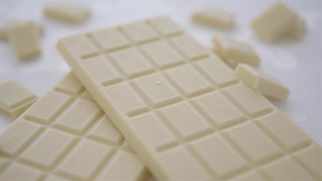 cube of white milk chocolate is being taken from white chocolate bar on white background close up