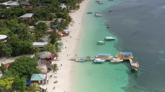 Aerial along island white sand beach with dive boats leaving, Roatan