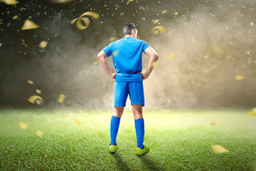 Fototapeta na wymiar Rear view of Asian football player man in blue jersey standing with flying golden confetti