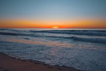Abstract seascape. Beautiful tropical beach at sunset. Blue ocean, colorful sky, and sun setting down the horizon