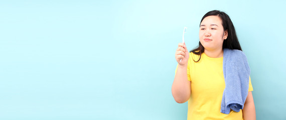 portrait of Asia woman with pouting lips, brushing her teeth isolated over blue background with copy space in studio, sad female standing in  holds  toothbrush.