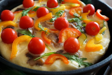 Traditional italian omelet with vegetables  fritatta with peppers, tomato and ruccola  in a cast iron pan during cooking close up 