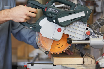 Close-up of young carpenter cutting wooden detail with electric saw in workshop