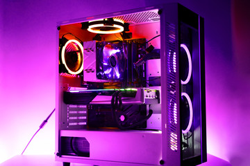 the new modern powerful gaming computer with beautiful rgb lights of different color and a glass case on the table in the dark