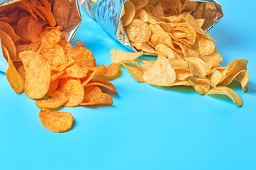 Many potato chips poured out of two shiny packagings on blue background. Space for text
