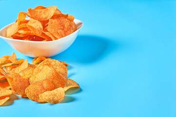White ceramic bowl full of potato chips on blue background. Space for text