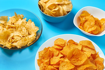 Plates and bowls full of spicy fried potato chips on blue background. Close-up