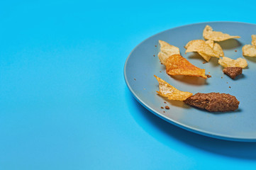 Malnutrition snack for beer spicy potato chips, pieces of rusk bread lies on blue table in sport bar or pub. Space for text