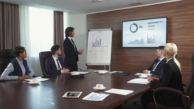 international business meeting, businessman speak at a meeting and shows financial infographic in the conference room, man in a suit communicates with colleagues, infographics on tv screen.