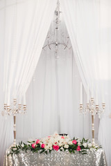 table with a tablecloth of silver sequins, two silver candelabra and a chandelier hangs over the table. Wedding decor for the bride and groom