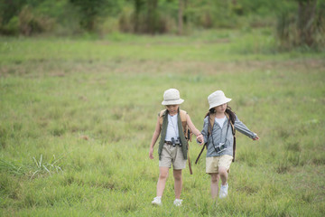 Two little girl carrying a backpack and wearing a hat. Running around in the grassland Children walk and enjoy the surrounding nature. She enjoys traveling in the summer. travel and adventure concept.