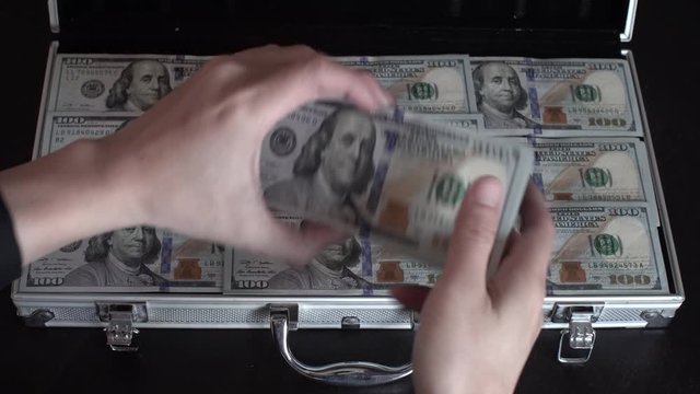 Popping open a brief case of $100 USD and flipping through it.