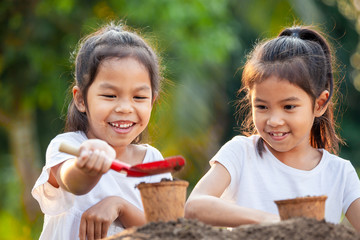 Two asian child girls prepare soil for planting young seedlings in recycle fiber pots together in the garden with fun