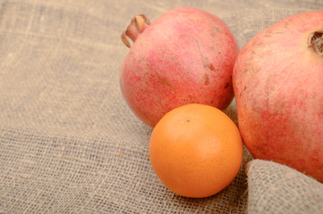 Two ripe pomegranates and tangerines on a background of rough homespun fabric close-up. Fitness diet. Healthy diet.