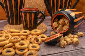 Small bagels, brown sugar, a mug of tea and ceramic dishes on a wooden background close-up.